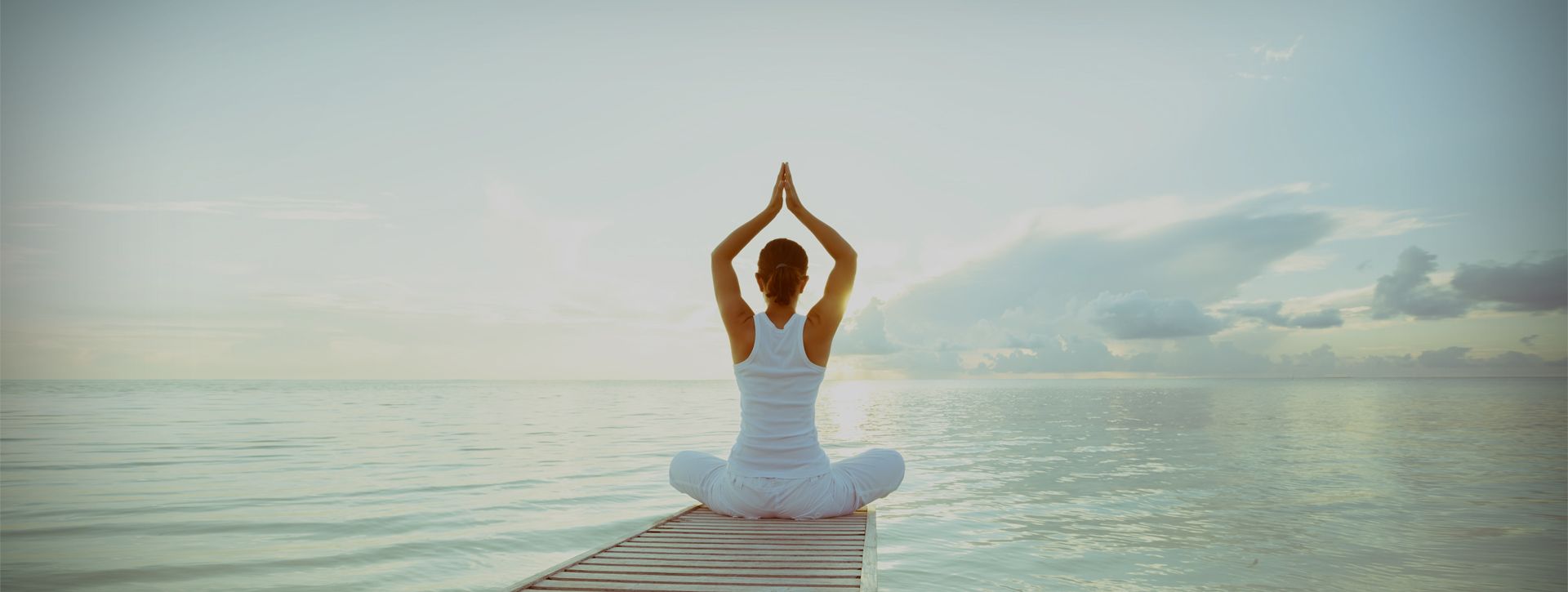 Female in all white practicing yoga on a pier looking out to the ocean